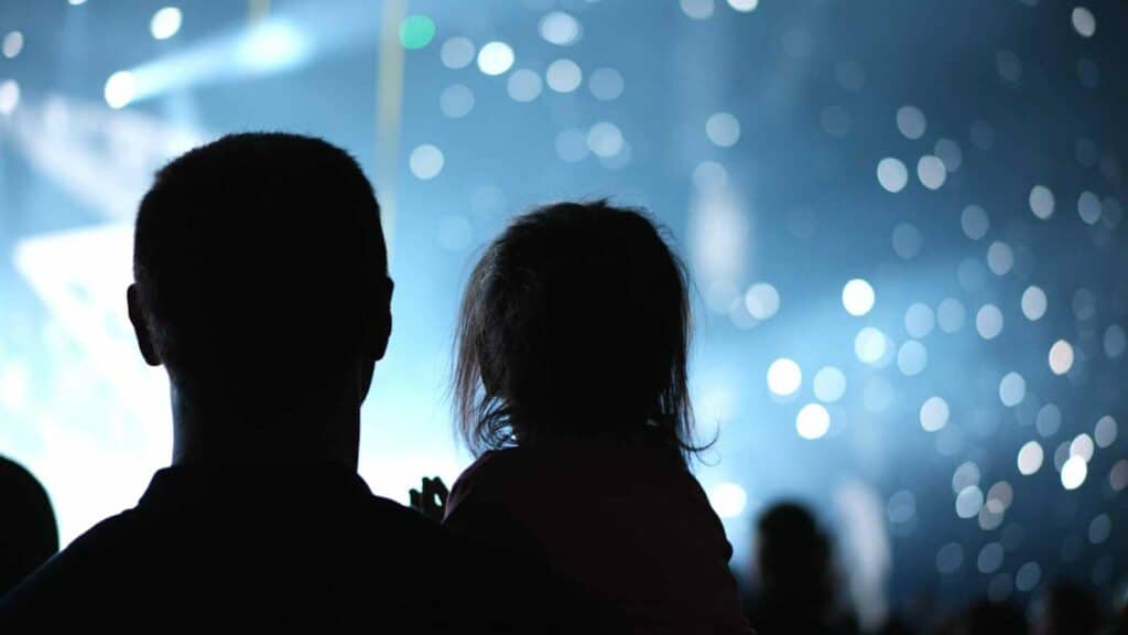 Silhouettes of two people watching a sumo event with bright lights and bokeh background.