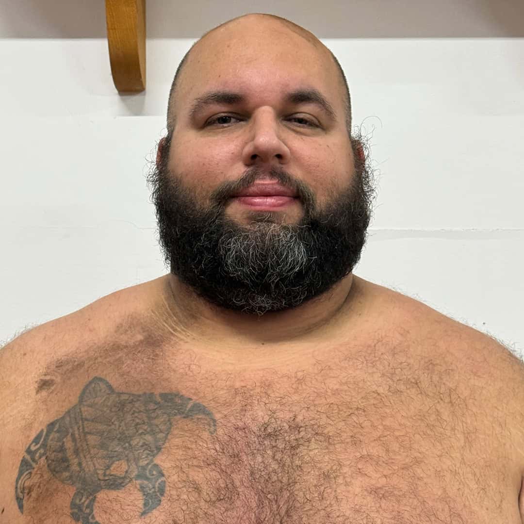 Sumo wrestler with a beard and tattoo on his chest.