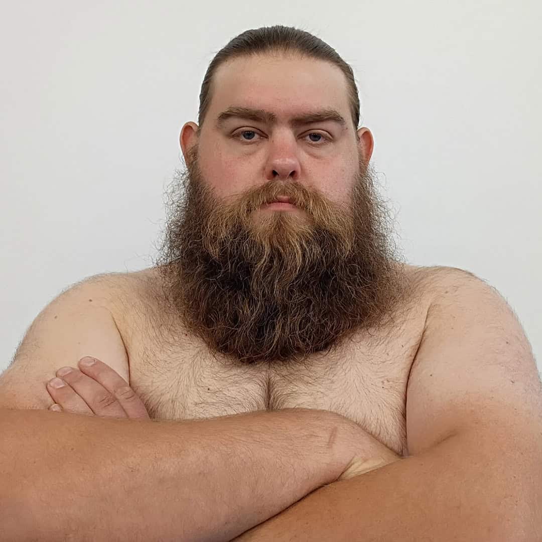 Sumo wrestler with long beard and crossed arms, shirtless, against a plain background.