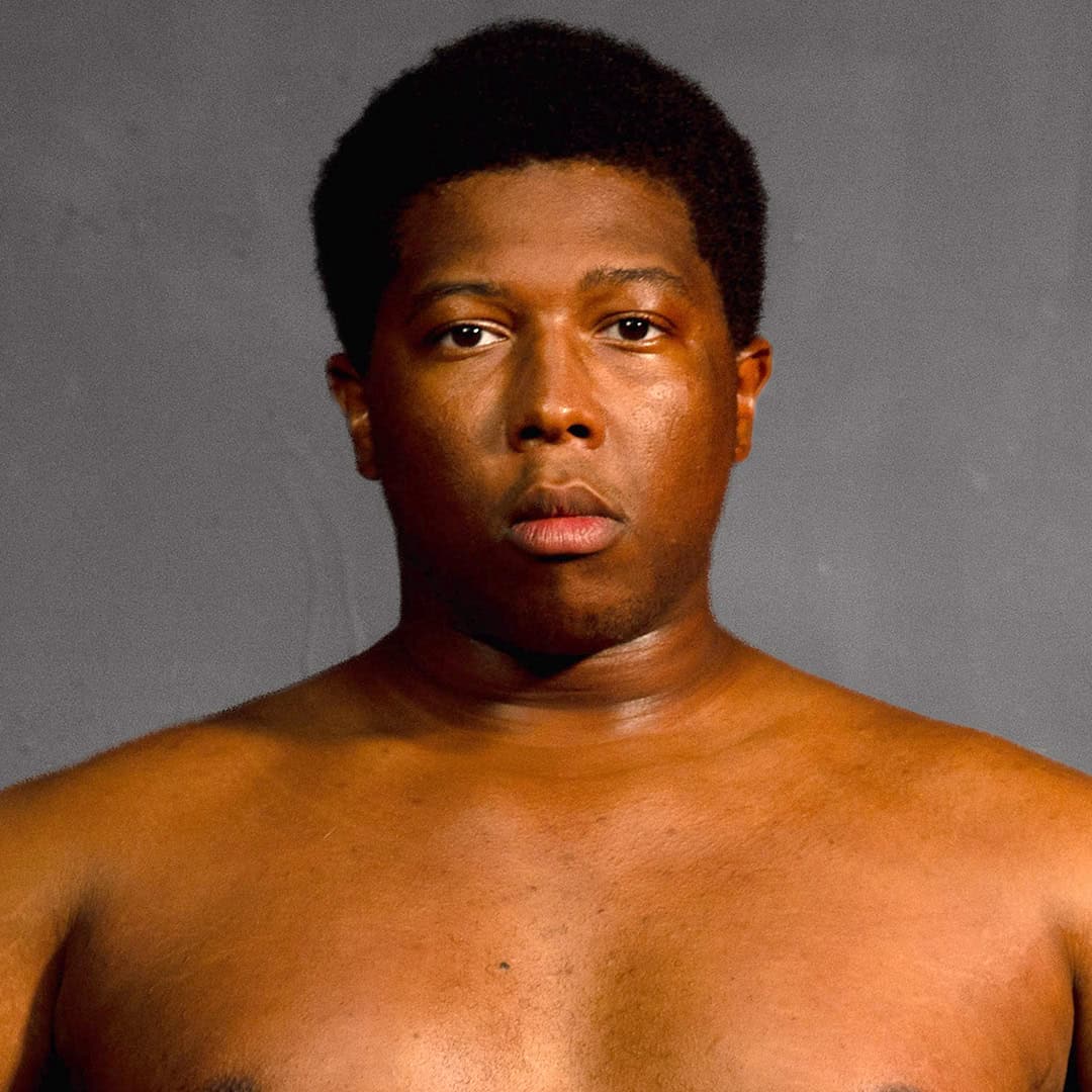 Close-up of a young man with natural hair and serious expression.