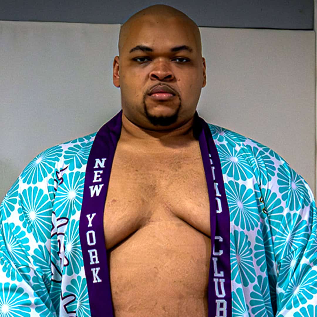 Sumo wrestler wearing a blue floral kimono with a purple sash.