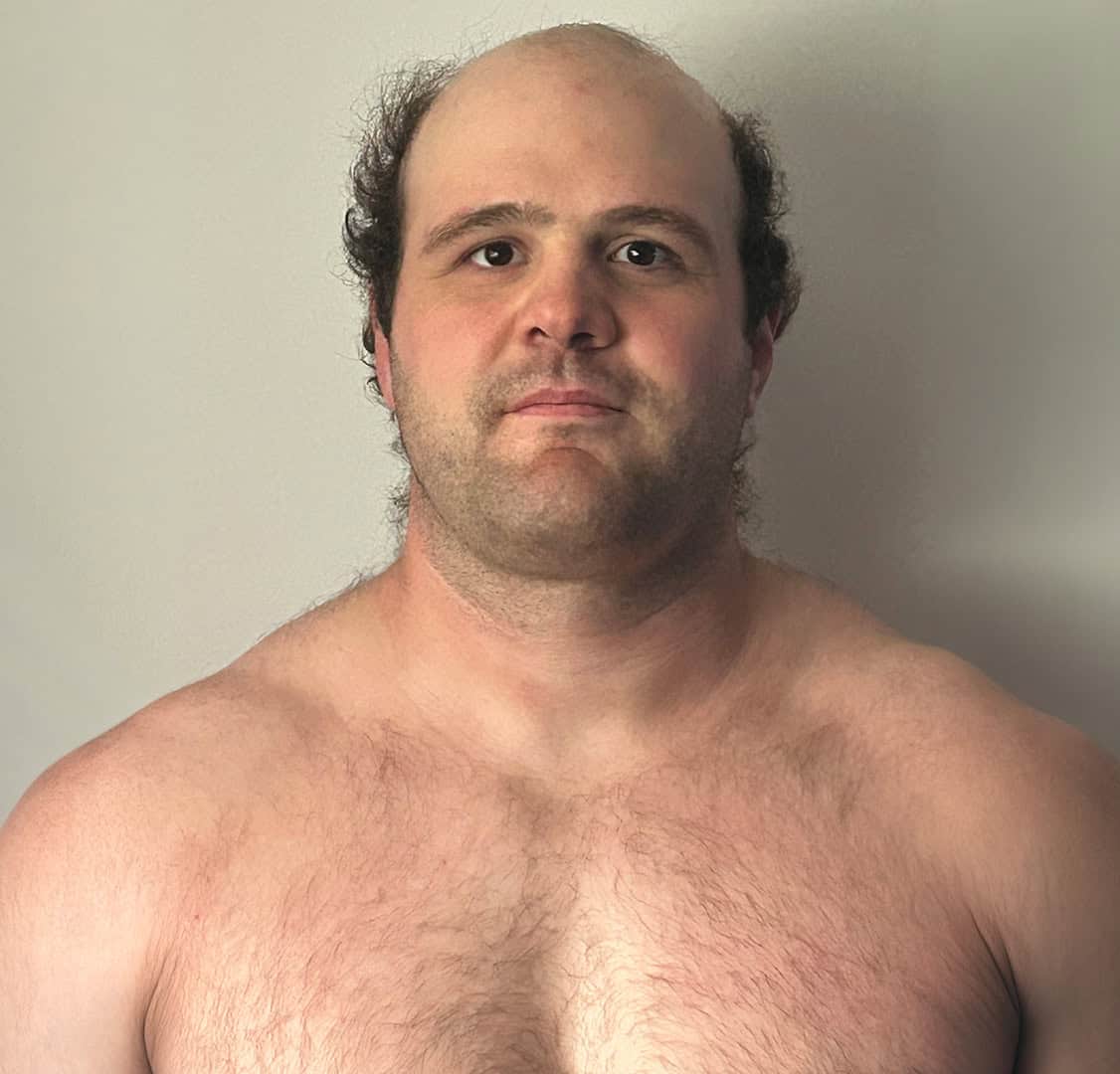 Man with a serious expression, no shirt, short hair, and a plain background.