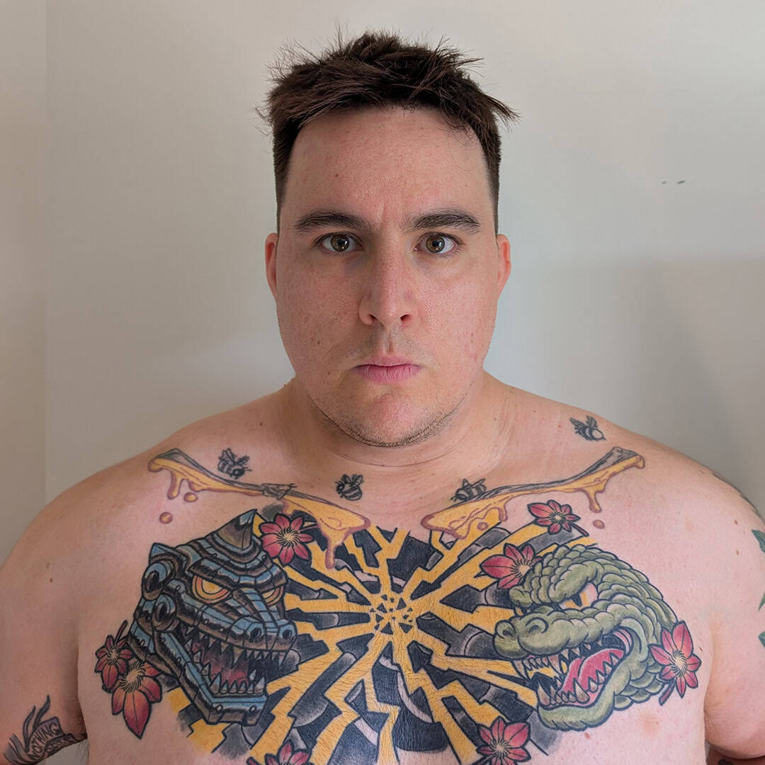 Man with tattoos on chest and shoulders, looking at camera.