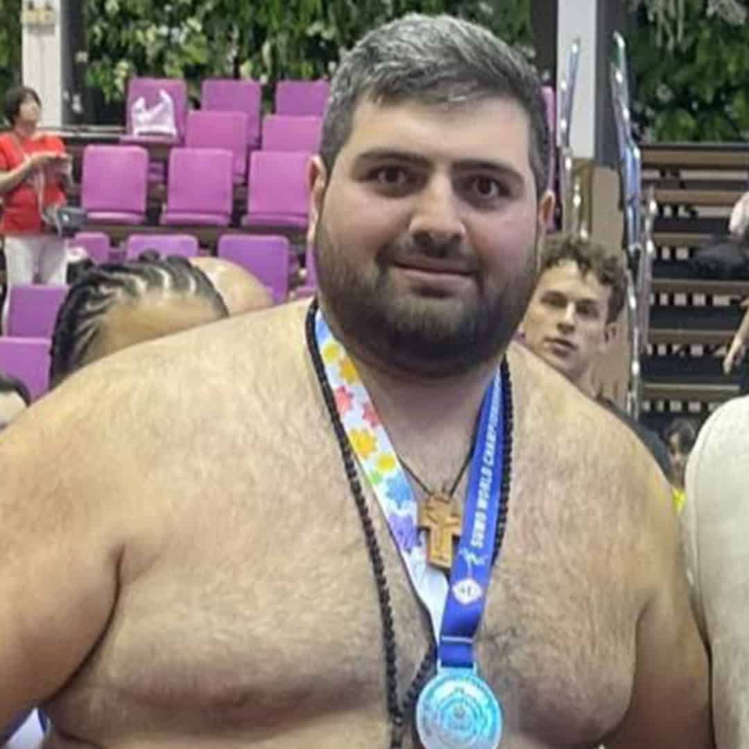 Sumo wrestler with medal at competition, smiling, in a sports arena.