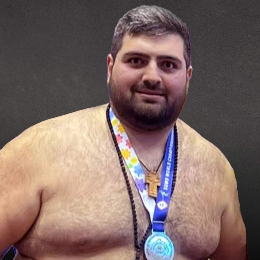 Sumo wrestler with medal and cross around neck, smiling at camera.