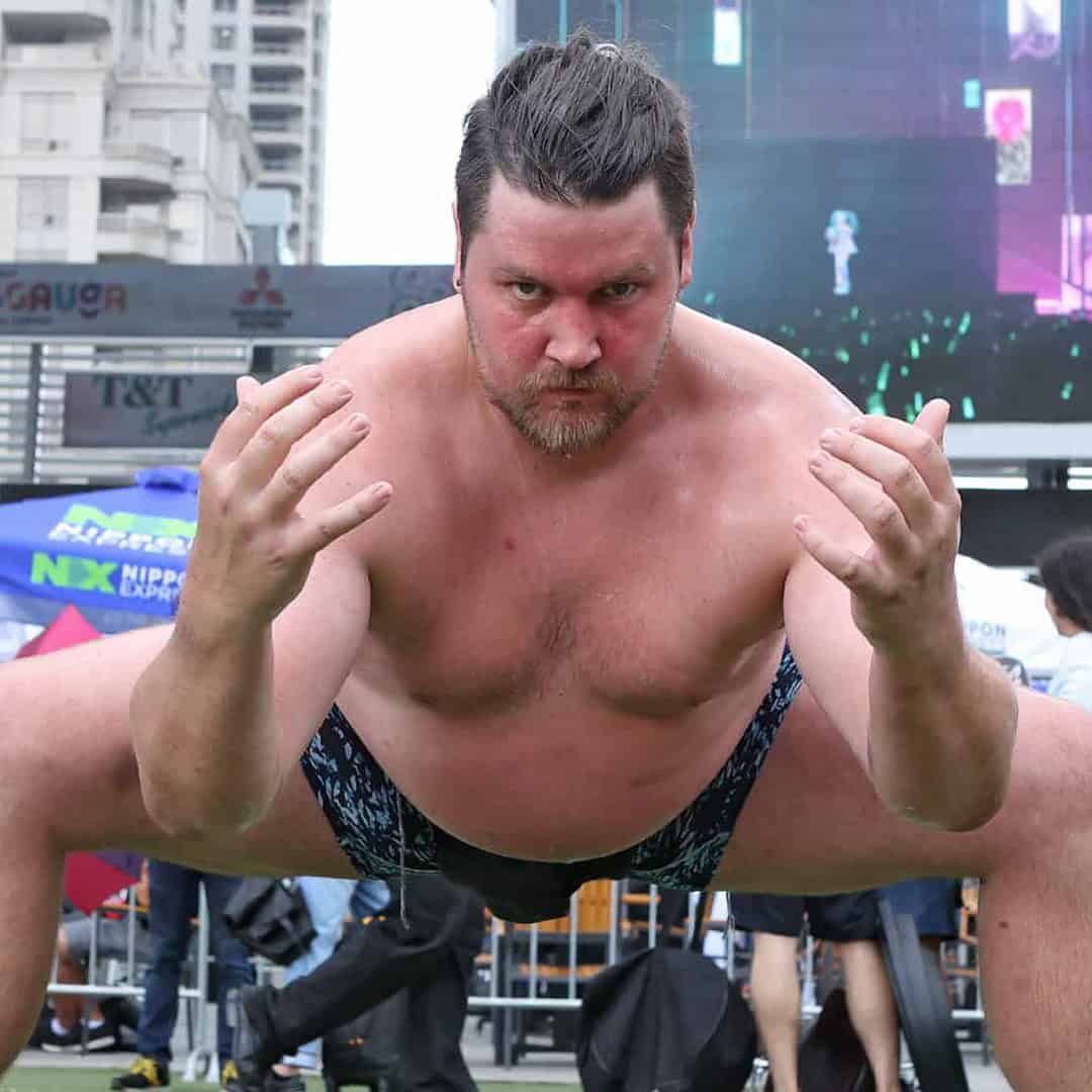 Sumo wrestler performing a push-up in an outdoor setting.