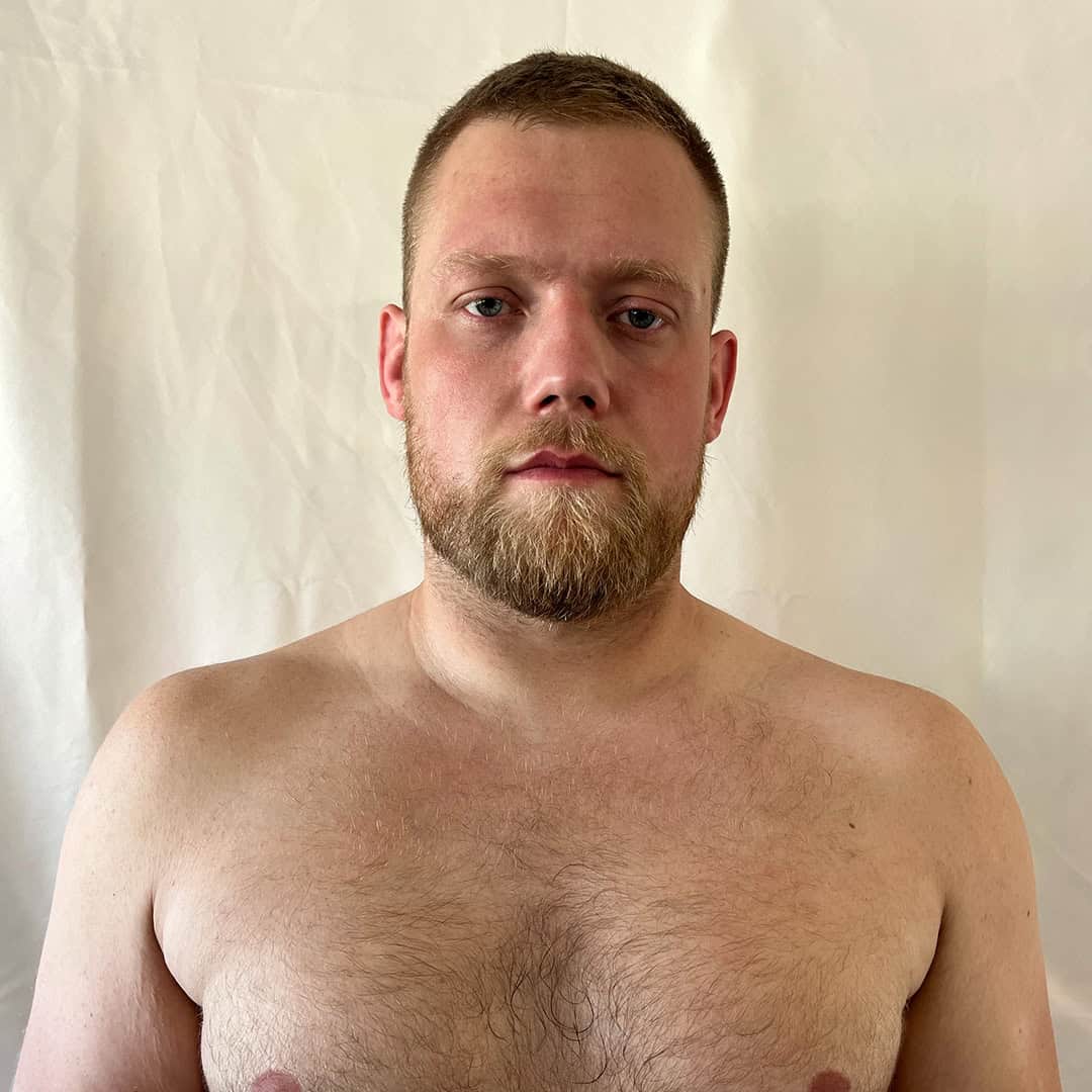 Shirtless man with short hair and beard looking at camera.