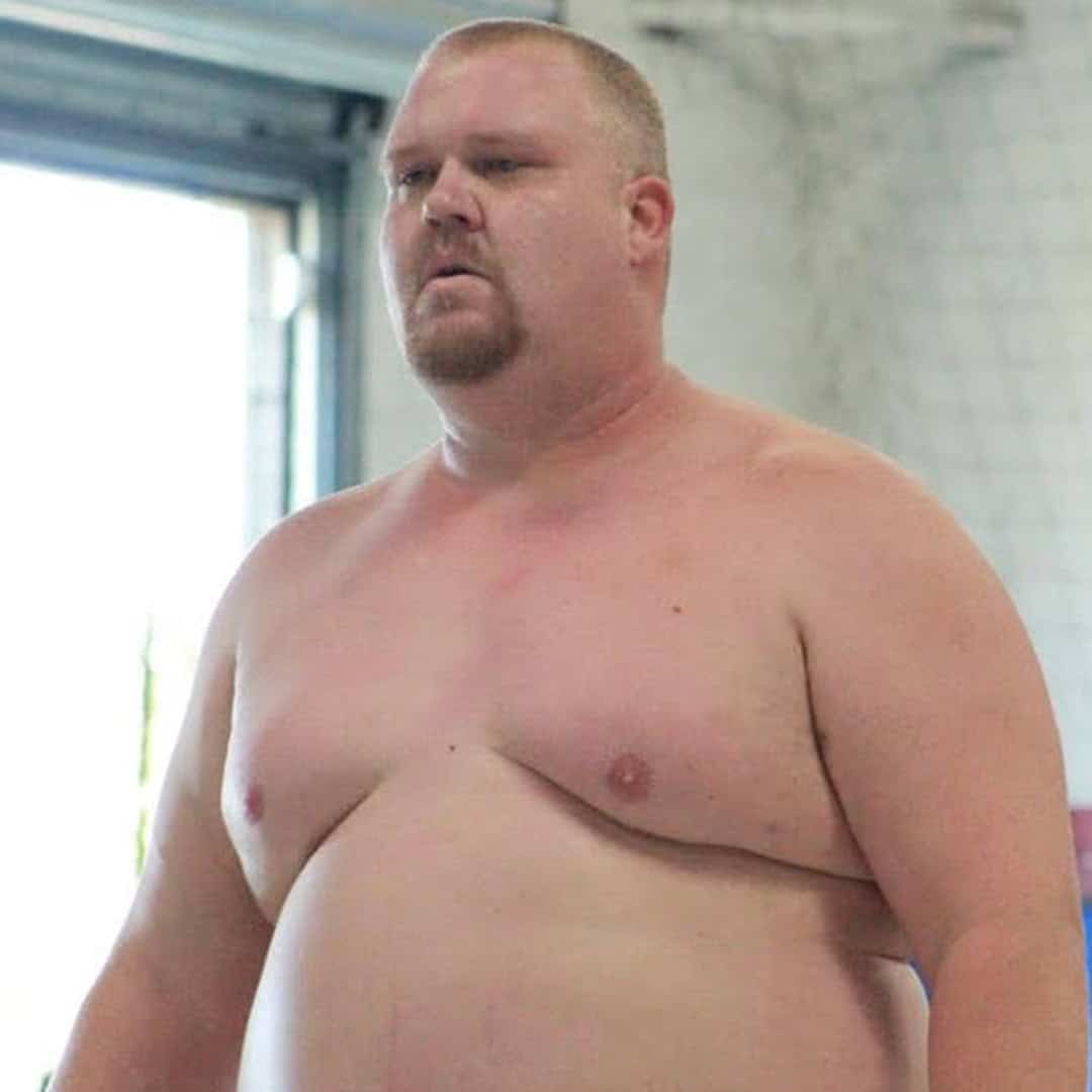 Sumo wrestler standing in training area, shirtless and focused.