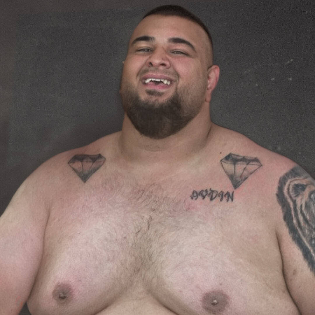 Smiling shirtless man with tattoos on chest and arm.